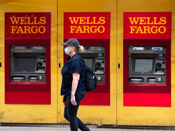 A masked woman walking past a few Wells Fargo ATMs.