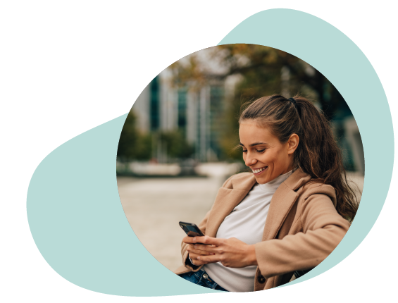 A smiling woman sitting outside and using her mobile device.